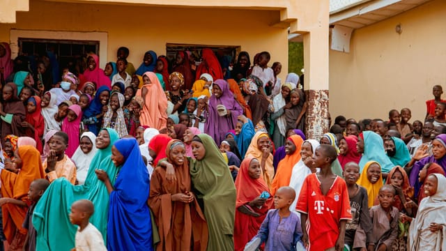 A vibrant crowd in colorful attire gathered outdoors in Borno, Nigeria, sharing happiness.