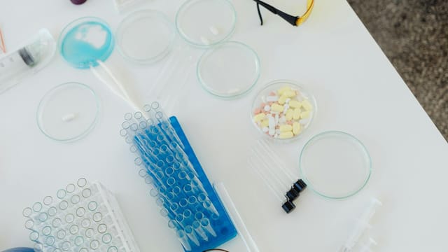 Aerial view of laboratory equipment including petri dishes, pills, test tubes, and syringes.