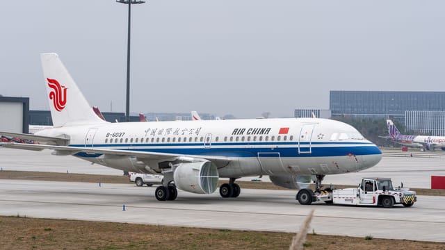 Air China plane on runway with ground support vehicle at a modern airport.