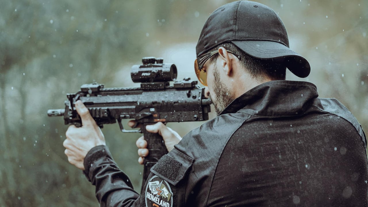 Man aiming with tactical gear and firearm in an outdoor setting during rain.