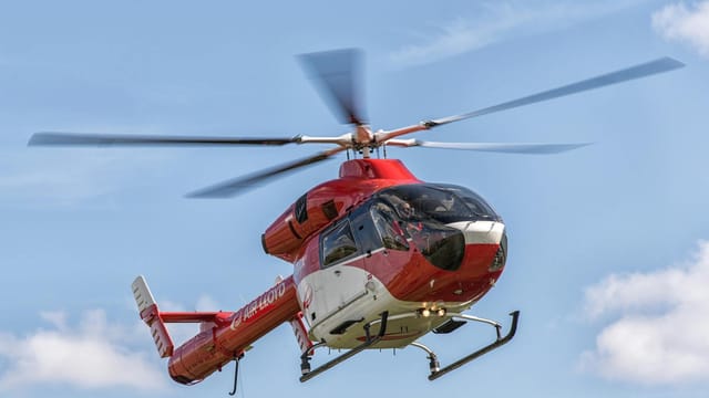 A red helicopter from Air Lloyd flying against a clear blue sky in Hamburg, Germany.