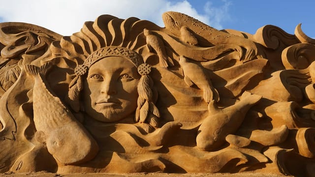 Detailed sand sculpture depicting a face and marine life in Søndervig, Denmark.