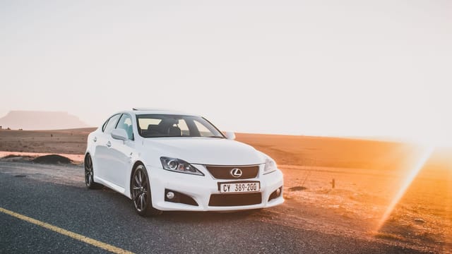 A sleek white sedan parked on an open road during sunset with a dramatic sky.