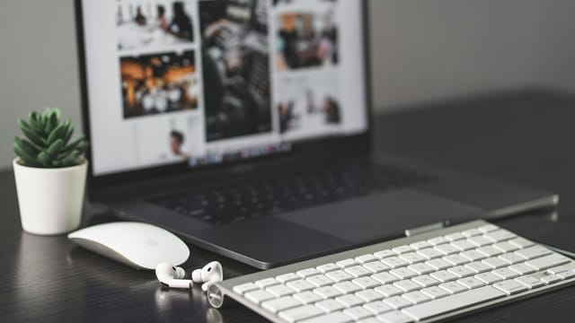 A sleek modern workspace featuring a laptop, keyboard, mouse, AirPods, and a small plant.