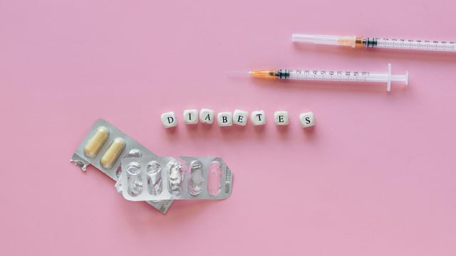 Flat lay of diabetes medication symbolized with pills and syringes on a pink background.