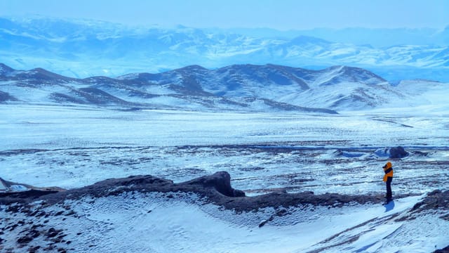 Expansive snow-covered landscape in Qinghai, China, with solitary person in winter attire surveying the scene.