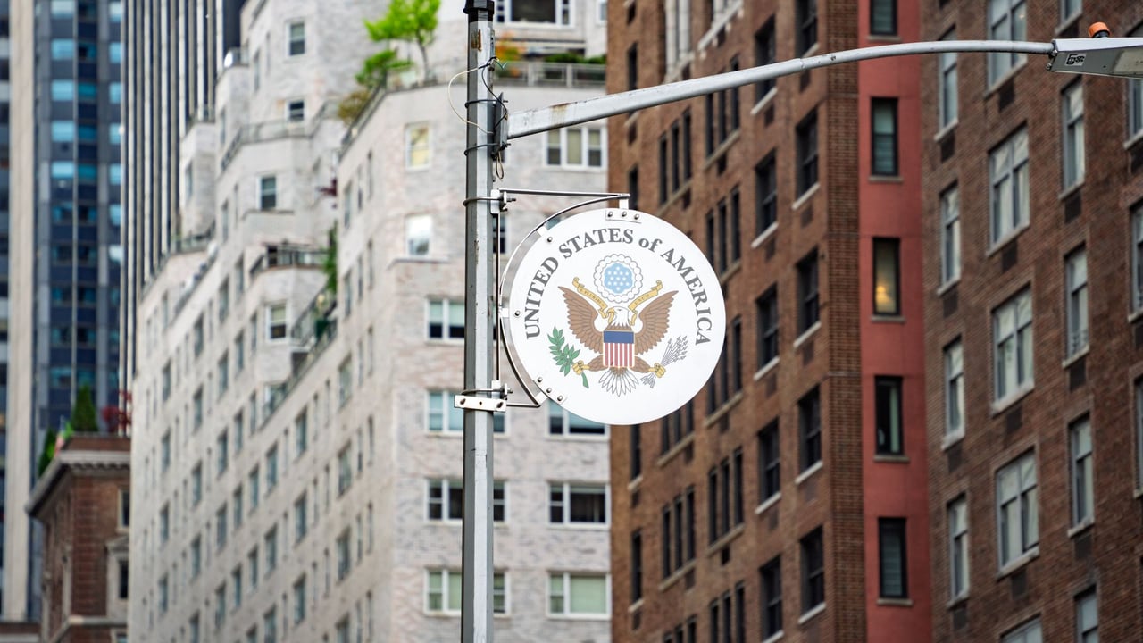 Street view of the US Embassy sign with New York City architecture in the background.