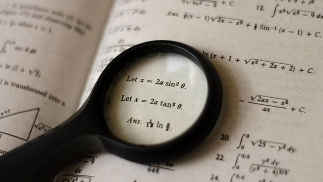 A magnifying glass focusing on mathematical equations in a textbook, symbolizing detailed study.