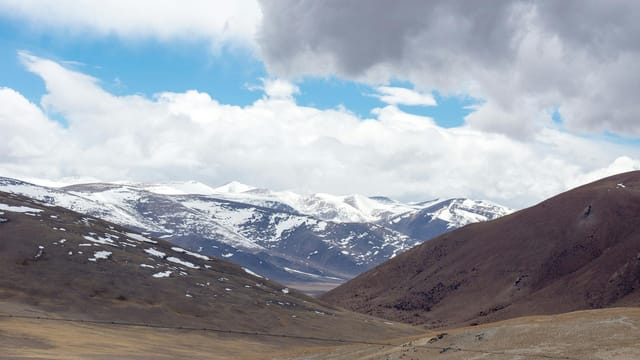 Breathtaking view of snow-capped mountains under a cloudy sky in Ngari, Tibet, showcasing natural beauty.