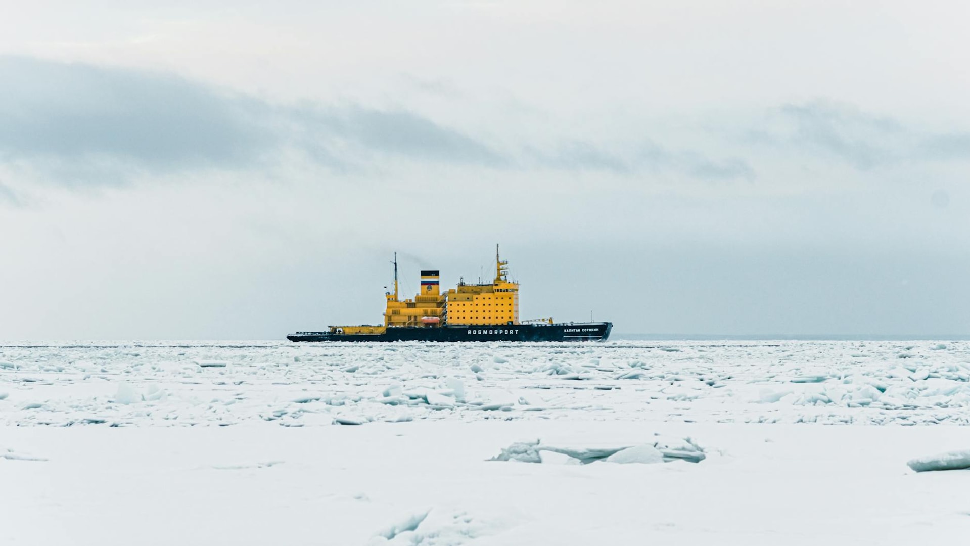 A yellow icebreaker ship sails through frozen waters near Saint Petersburg, Russia, in winter.