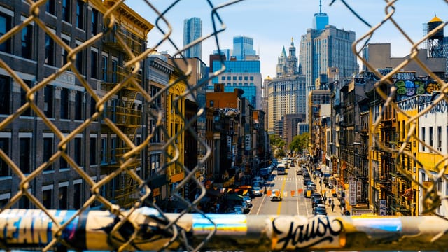 Explore a vibrant urban scene through a chain-link fence, capturing New York City's lively streets.