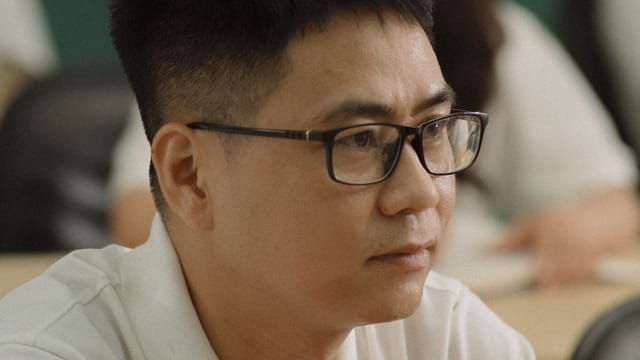 A focused man wearing eyeglasses looks ahead thoughtfully.