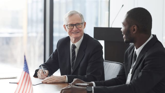Two business professionals discussing and signing documents at a meeting with an American flag on the table.