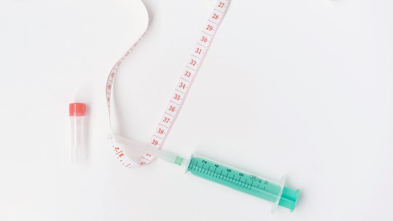 Flat lay of medical supplies with tape measure and syringe on white background, symbolizing healthcare.