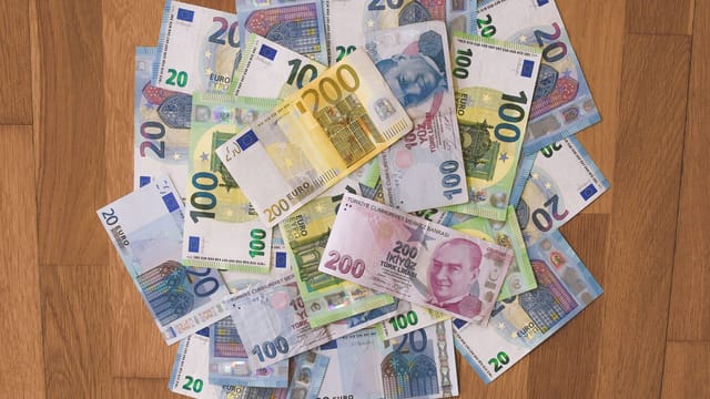 A pile of Euro and Turkish Lira banknotes scattered on a wooden surface, showcasing various denominations.