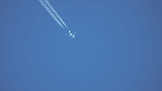 A high-flying airplane with contrails against a vibrant blue sky captured mid-flight.