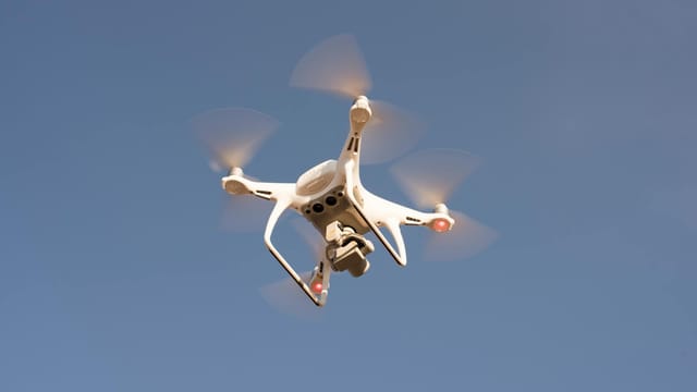 A white drone in flight against a clear blue sky, capturing aerial footage with precision.