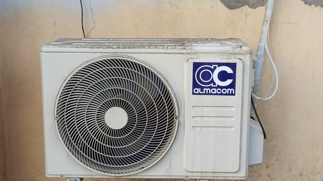 A well-used outdoor air conditioning unit affixed to a brick wall, showcasing urban climate control.