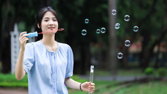 A woman enjoys blowing bubbles in a lush Vietnamese park, expressing joy and playfulness.