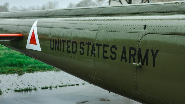 Detailed view of a U.S. Army helicopter tail with military markings, taken outdoors on a rainy day.
