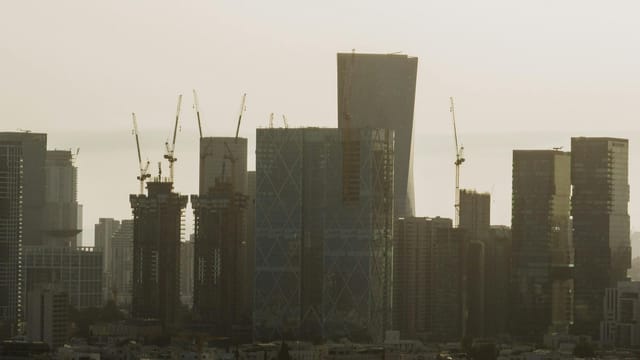 A view of Tel Aviv's cityscape featuring skyscrapers and construction cranes under a hazy sky.