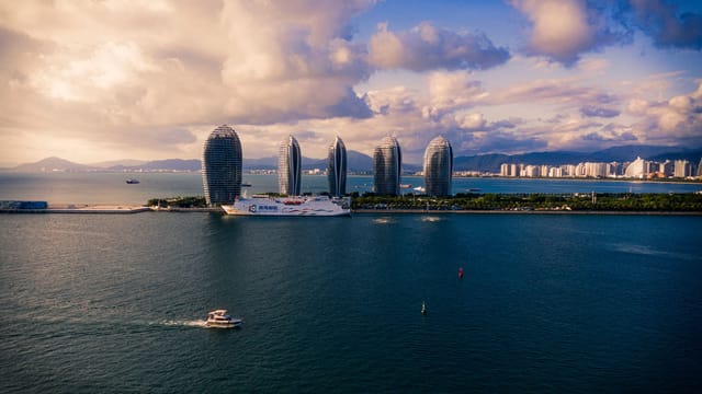 Modern cruise ships and boats floating on calm sea against cloudy sky near futuristic skyscrapers located on Phoenix Island in China