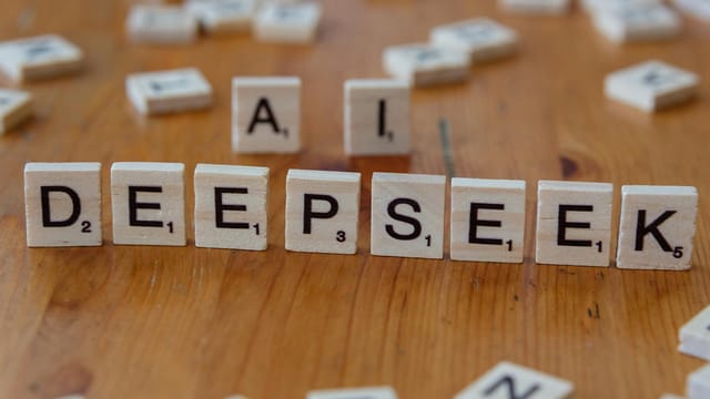 Wooden Scrabble tiles spelling 'DEEPSEEK' with 'AI' on a wooden table, illustrating AI concepts creatively.