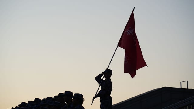 A soldier salutes with a flag during a parade at sunset, creating a striking silhouette.