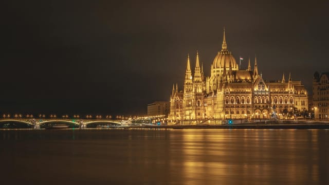 Stunning view of the illuminated Hungarian Parliament Building by the Danube River in Budapest at night.