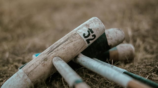 Stack of wooden croquet mallets on grass, showcasing sporting equipment.