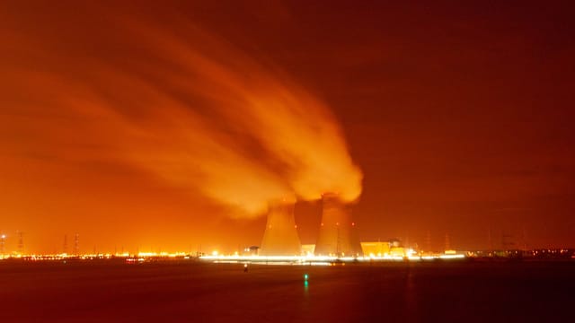 A dramatic view of cooling towers emitting steam against an orange night sky, showcasing industrial energy production.