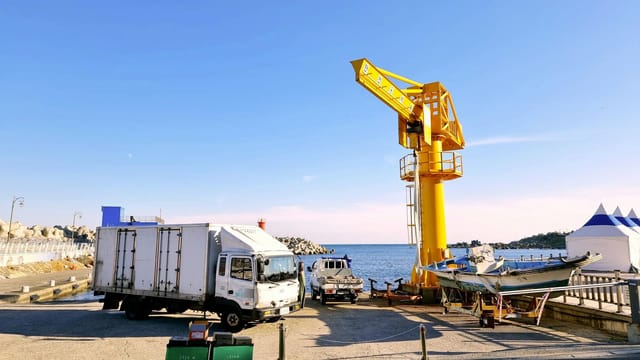 Colorful harbor scene in Busan featuring a yellow crane, trucks, and sea view.