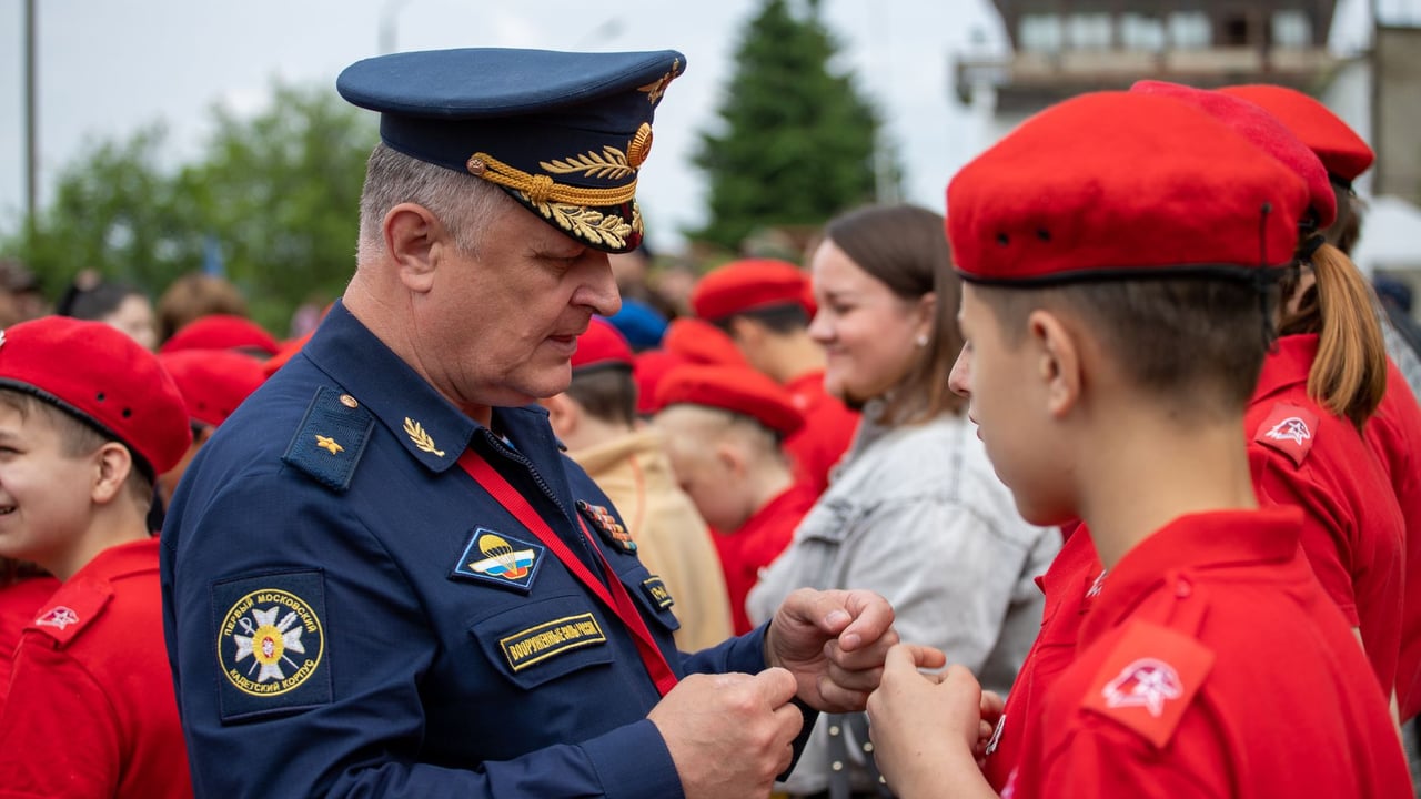A military officer engages with youth cadets in uniform at an outdoor event.