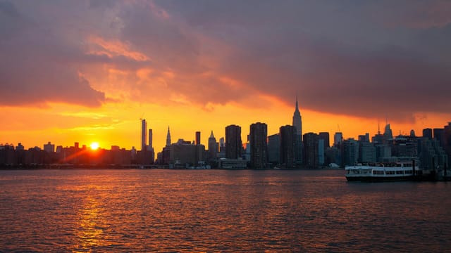 Stunning view of New York City skyline at sunset, featuring vibrant orange hues over the skyline and water.