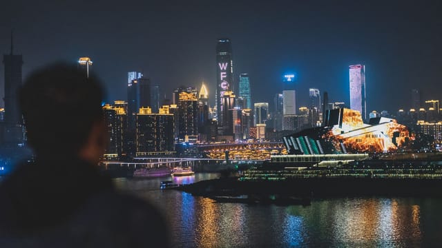 Back view unrecognizable blurred male enjoying amazing view of contemporary illuminated embankment in Chungking China during night