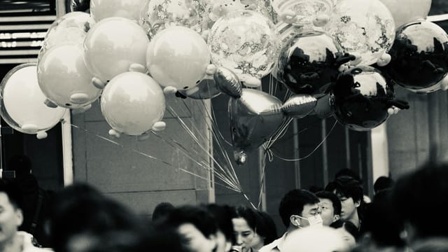 A bustling urban scene in black and white featuring a crowd with decorative balloons in Xi An Shi, China.