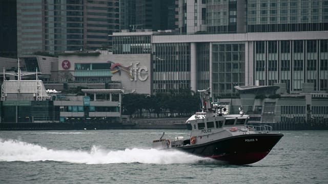 Police boat in Hong Kong harbor against the skyline, featuring iconic IFC building.