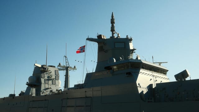 A Norwegian navy frigate with a national flag in daylight.