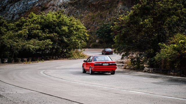 Illustrative image: A red car driving on a scenic mountain road in Mangatarem, Philippines, surrounded by greenery and hills.