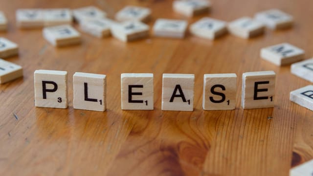 Scrabble tiles arranged to spell 'Please' on a wooden surface, symbolizing politeness.