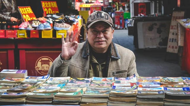 An elderly vendor selling books at a vibrant Tianjin street market.