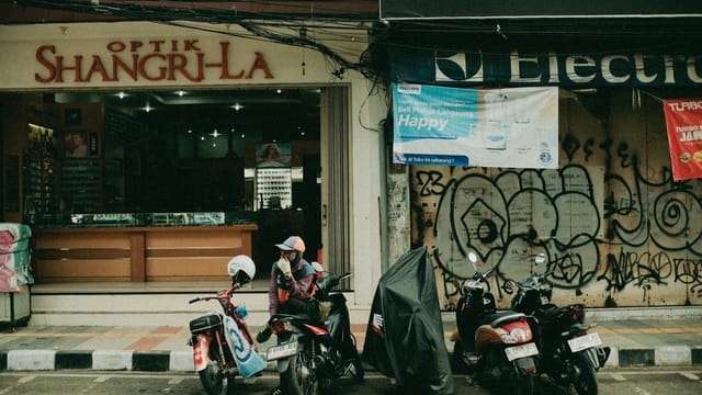 Urban street scene featuring parked motorbikes outside an optician in Jakarta, Indonesia.