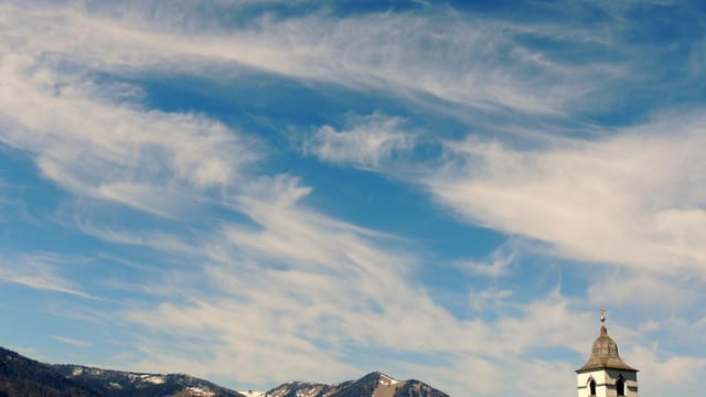 Church tower against Salzkammergut mountains with a vivid blue sky.