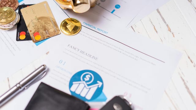 Close-up of financial documents, credit cards, coins, and a pen on a wooden desk.