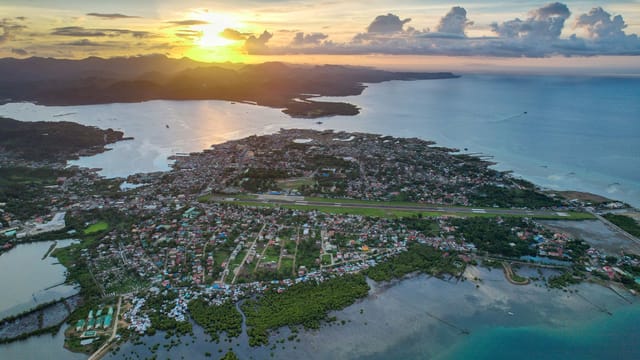 Scenic aerial panorama of Masbate City, Philippines during a vibrant sunset with ocean and landscape views.
