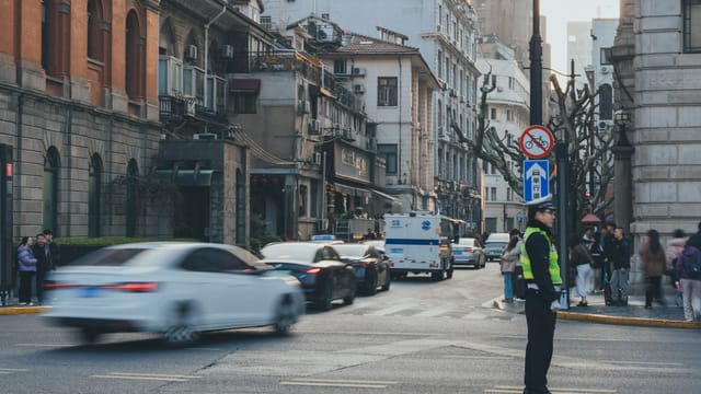 An urban street bustling with cars and people, featuring a traffic officer directing vehicles in a vibrant cityscape.