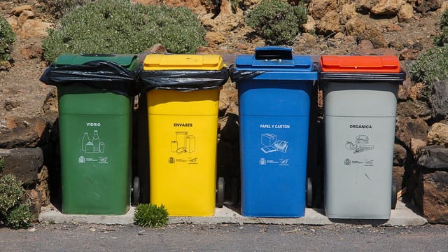 Four recycling bins for glass, packaging, paper, and organic waste outdoors.