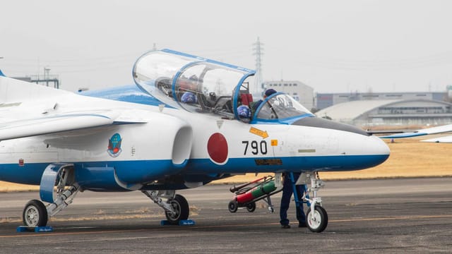 Training jet with Japanese insignia taxiing for preparation on airfield.