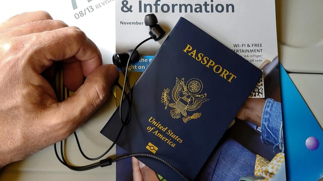 Close-up of US passport with inflight magazine and headphones on an airplane seat, ready for travel.