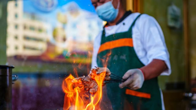 A street food vendor grills meat skewers outdoors in Qinghai, China, showcasing local culinary traditions.